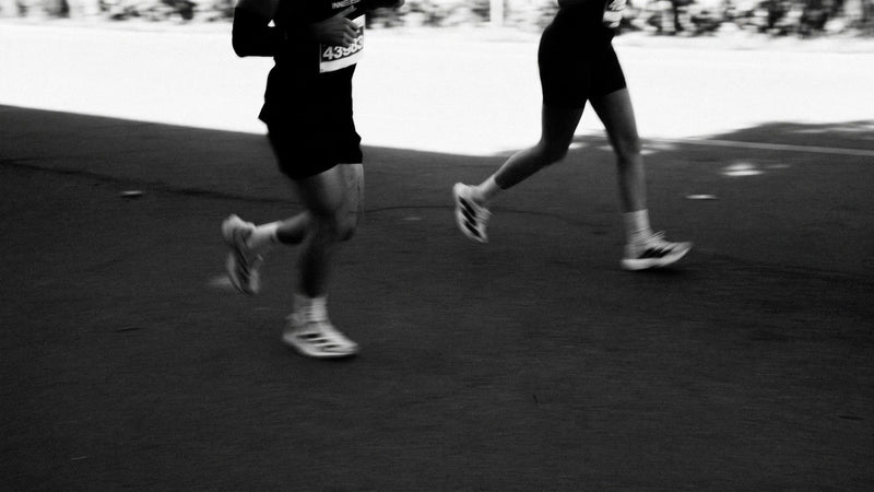 Black and white close-up of two runners' legs and race bibs mid-stride