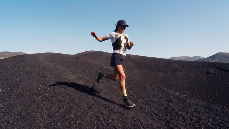 Woman running downhill on a black volcanic ridge under a blue sky