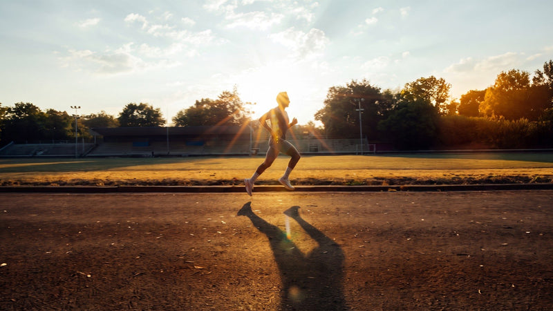Runner silhouetted against a low sun on a dirt track