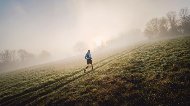 Runner climbing a misty hillside at sunrise in cold weather